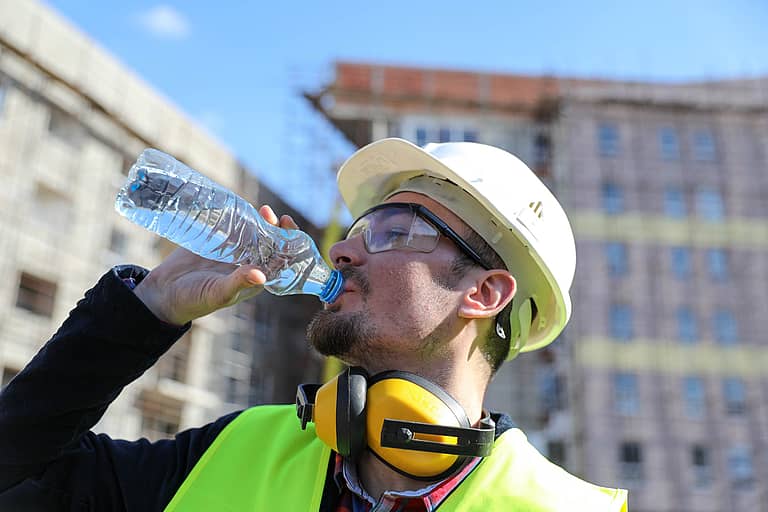Worker at construction site with bottle of water, close up. | Photo: Gabrijelagal | istock.com